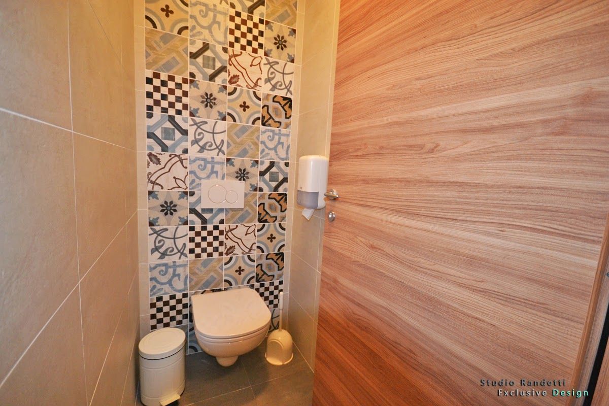 Piccolo bagno con WC, parete rivestita con piastrelle decorate, pavimento beige e porta scorrevole effetto legno.