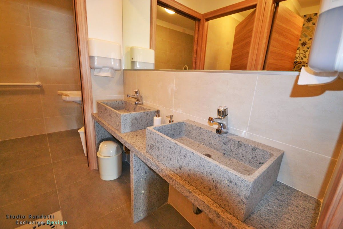 Bagno con doppio lavabo in pietra, specchio a parete, piastrelle beige e porta in legno.