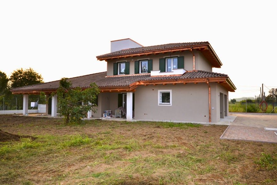 Casa a due piani con tetto di tegole e un piccolo portico, situata in un cortile erboso al crepuscolo.