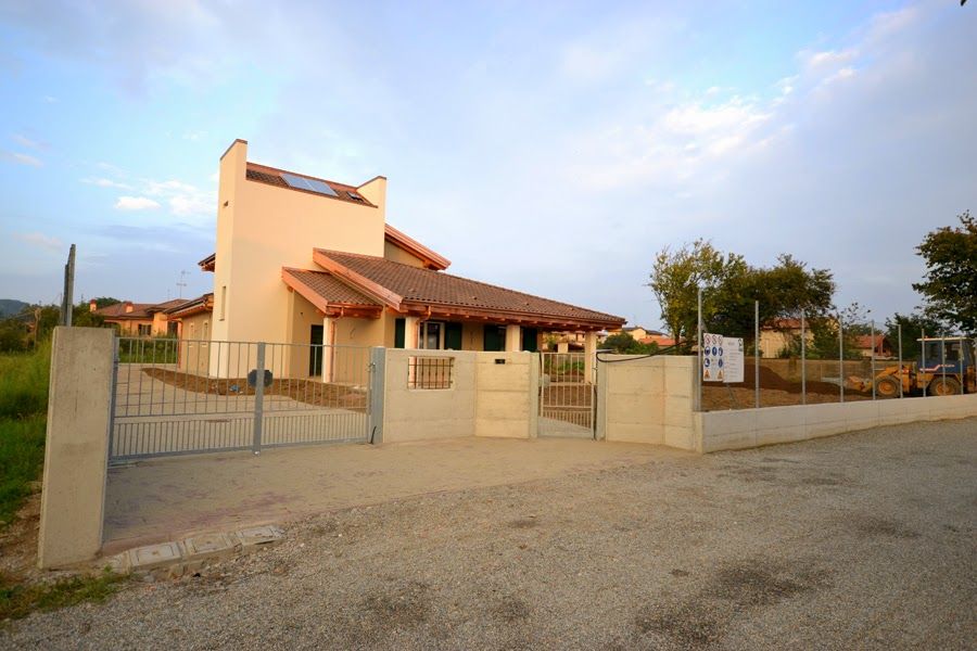 Casa a un solo piano con tetto rosso dietro una recinzione con cancello su una strada sterrata al tramonto