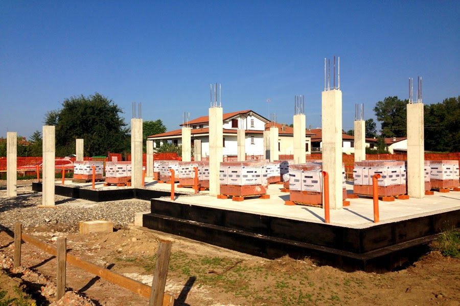 Fondamenta in costruzione con colonne in cemento e casseforme arancioni su un terreno sterrato.