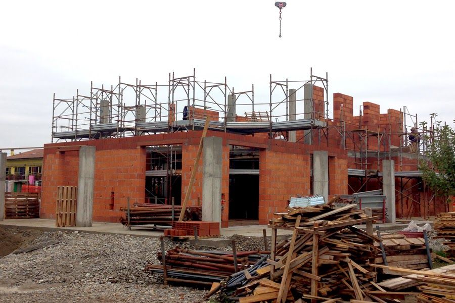 Edificio in mattoni in costruzione con impalcature e cataste di legname davanti.