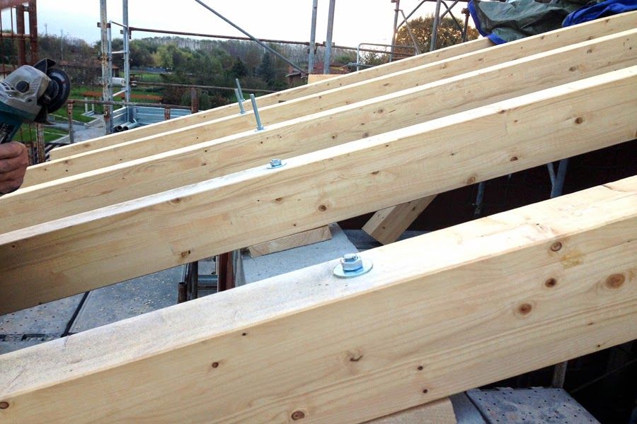 Travi del tetto in legno in fase di costruzione, con un operaio che utilizza un utensile elettrico sulla sinistra.