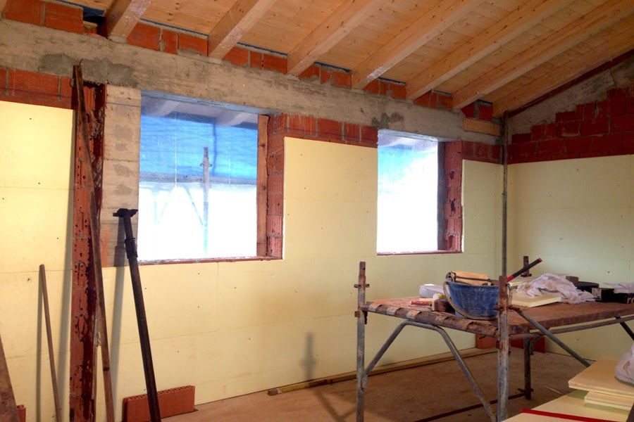 Stanza non rifinita con mattoni a vista, finestre e attrezzi da costruzione su un tavolo da lavoro.
