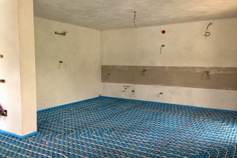 Cucina vuota e non rifinita con pavimento blu a motivi geometrici e pareti bianche, con tubature a vista.