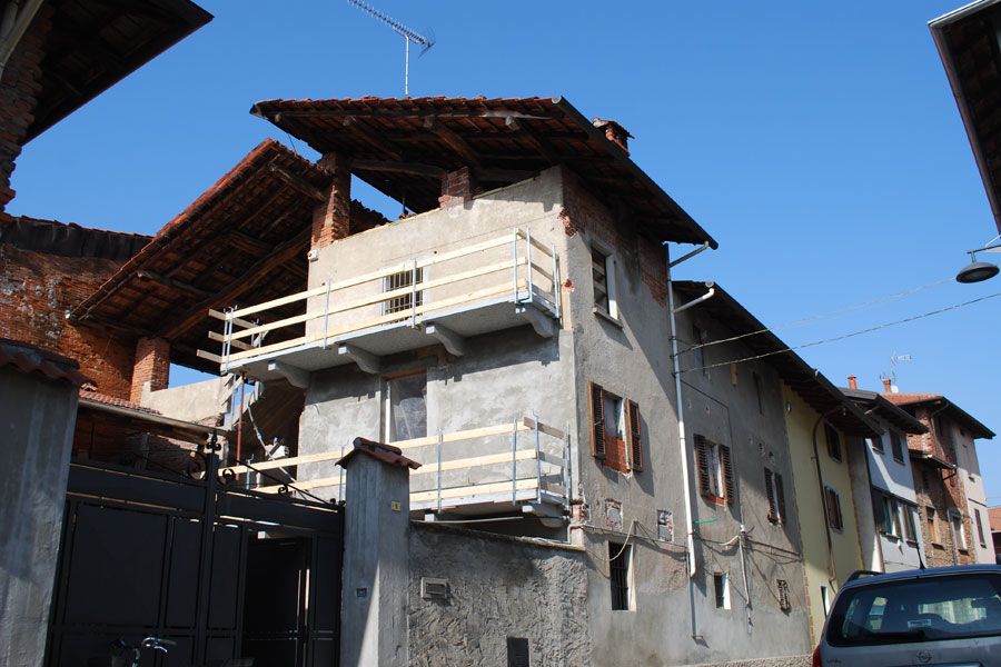 Vecchia casa in pietra con balconi e finestre con persiane in una stradina stretta sotto un cielo azzurro