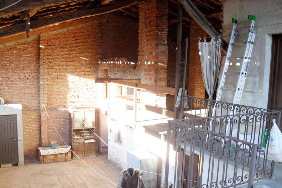 Soffitta luminosa con mattoni a vista, travi in legno, scala e ringhiera in metallo in un ambiente loft.