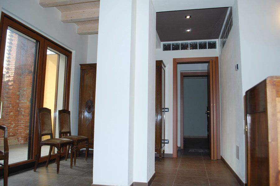 Interno di un corridoio moderno con scala, sedie in legno e alte finestre sulla sinistra.