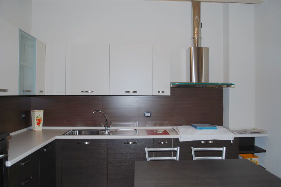 Cucina moderna con mobili bianchi, pensili inferiori scuri, lavello in acciaio inox e isola centrale nera.