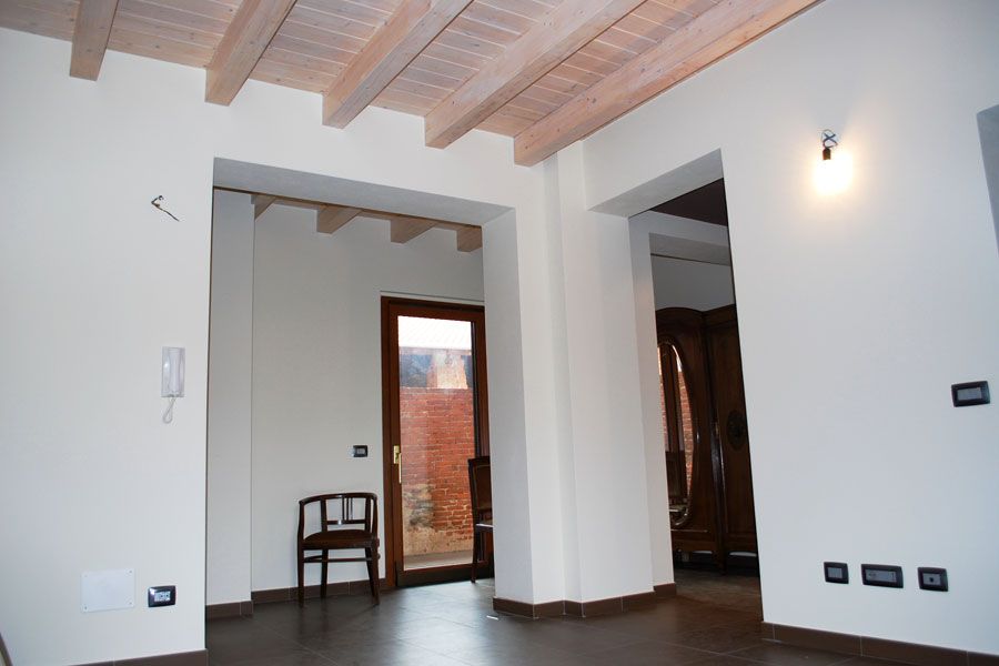 Stanza moderna vuota con pareti bianche, travi in legno a vista e pavimento scuro, vista attraverso una porta.