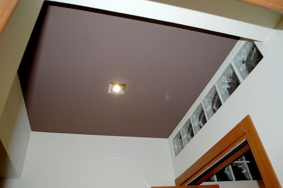 Soffitto ad angolo interno con pannello incassato marrone, luce a incasso e una finestra vicino all'angolo in alto a destra.