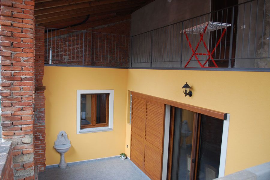 Balcone giallo nel cortile con porte in legno, piccola finestra, muro in mattoni e sedia rossa soprastante