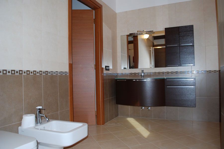 Bagno moderno con lavabo, specchio, doccia e pareti rivestite con piastrelle marroni.