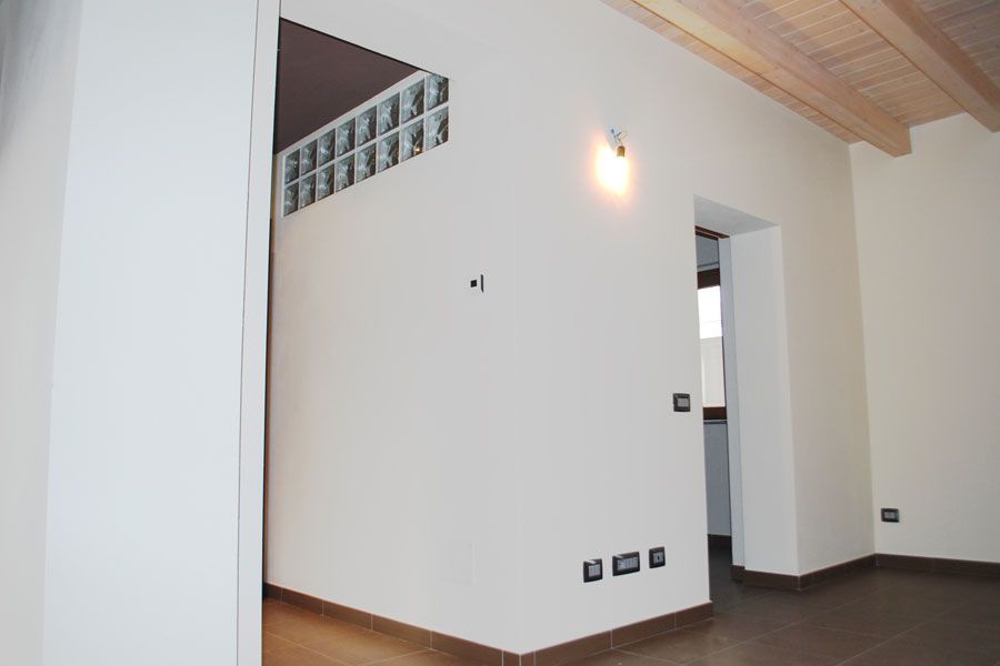 Stanza moderna vuota con pareti bianche, pavimento scuro, soffitto in legno e una porta che conduce a un'altra stanza.