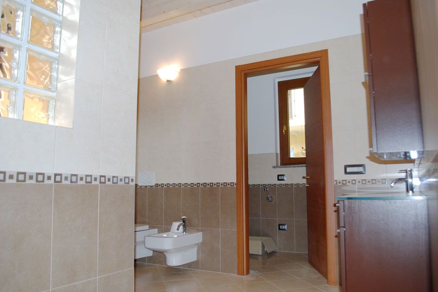 Bagno moderno piastrellato con bidet, lavabo e finiture in legno sulla porta.