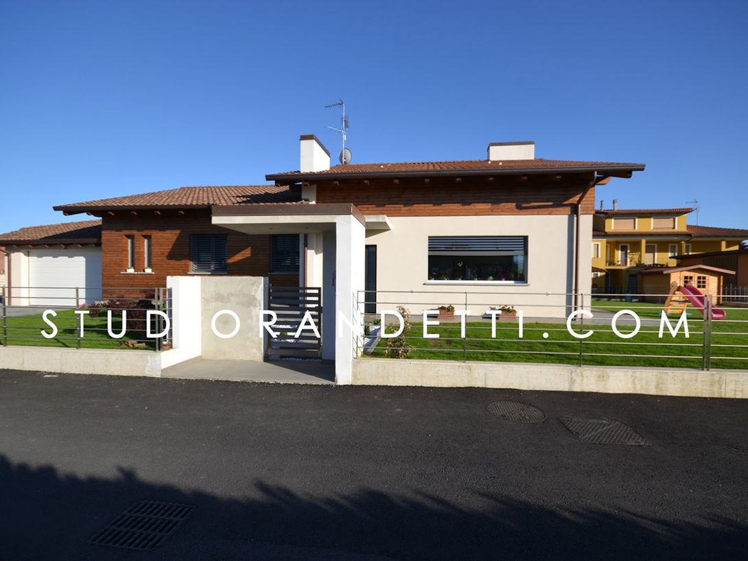 Casa moderna a un solo piano con pareti bianche, tetto marrone e cancello d'ingresso sotto un cielo azzurro limpido.