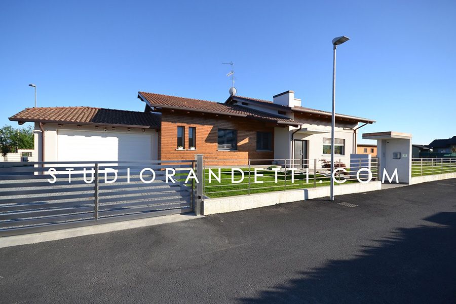 Casa moderna con esterni bianchi e in mattoni, giardino recintato e cielo azzurro limpido in una giornata di sole.