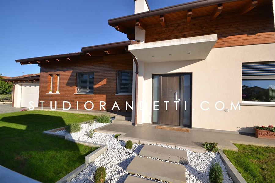 Esterno moderno di una casa in mattoni con tetto in legno, ampie finestre e vialetto d'ingresso curato.