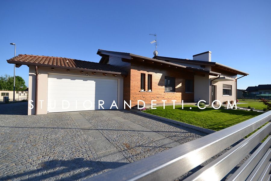 Casa unifamiliare moderna con garage bianco, facciata in mattoni e vialetto di accesso in ghiaia, esposta alla luce del sole.
