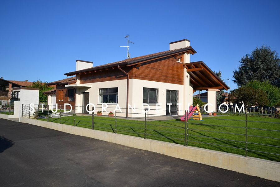 Casa moderna bianca con tetto rosso, prato verde e vialetto d'accesso sotto un cielo azzurro limpido.