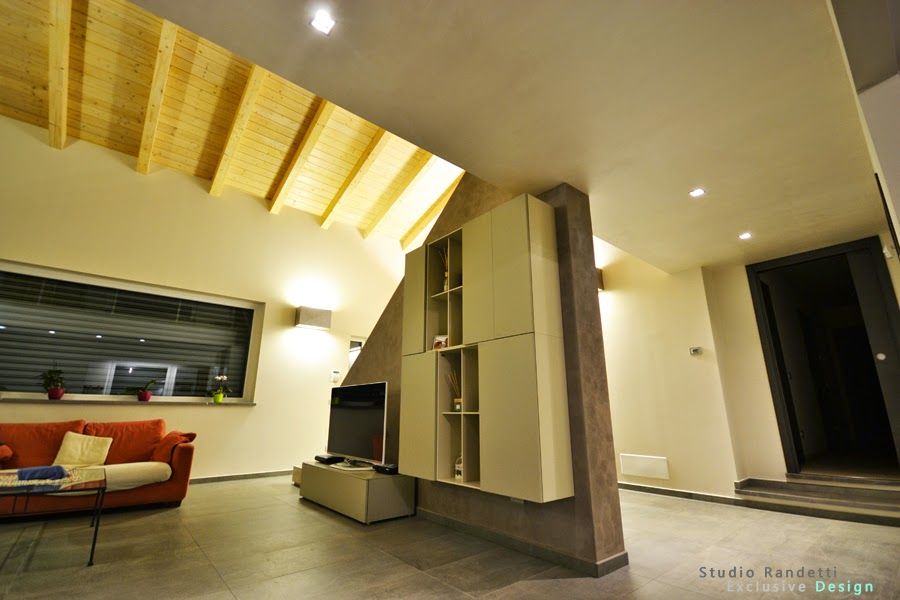 Soggiorno moderno con soffitto inclinato in legno, pareti beige, divano, TV e porta aperta.