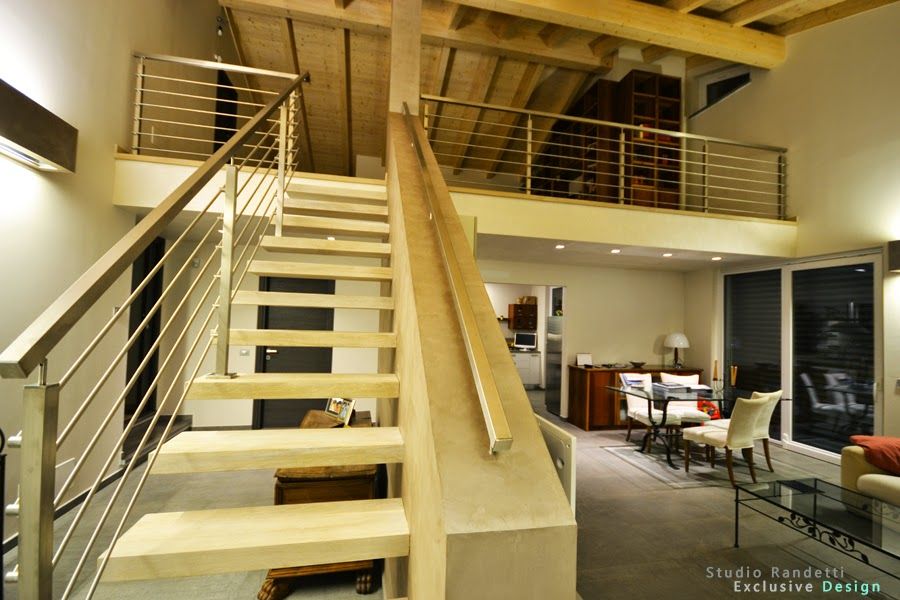 Interno di un loft moderno con scala a vista, travi in ​​legno e zona pranzo al piano inferiore.