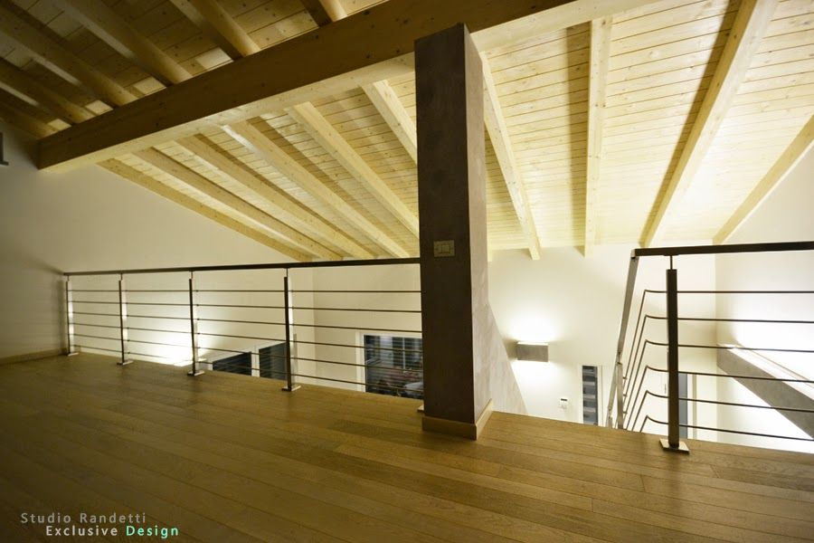 Interno di un loft moderno con travi a vista, pavimento in legno e ringhiera che si affaccia su un luminoso piano inferiore.