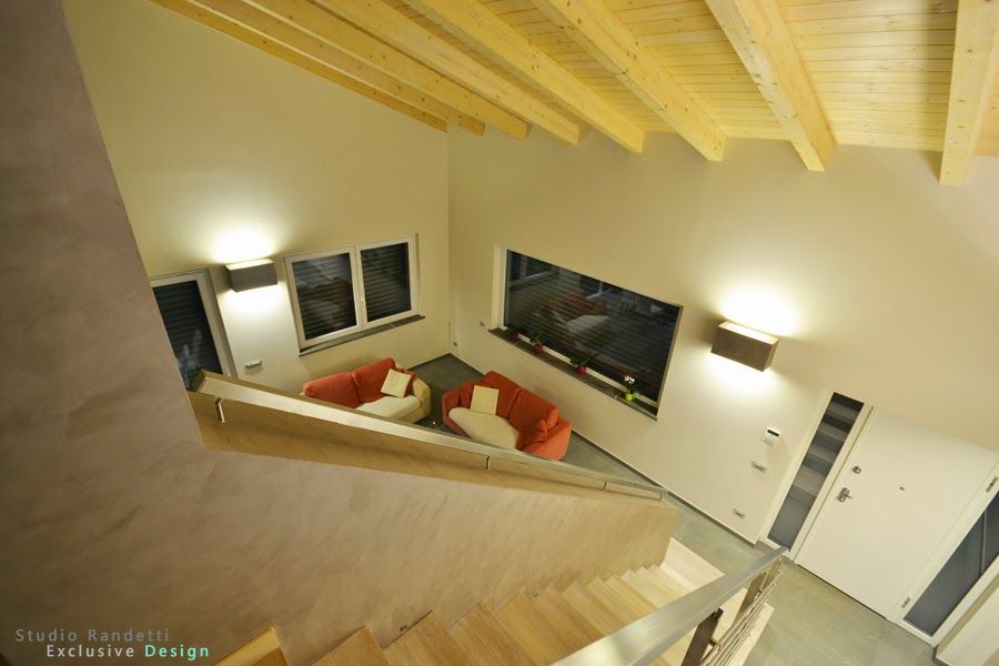 Soggiorno in stile loft moderno con pareti color beige, soffitto con travi a vista, scala e divani arancioni.