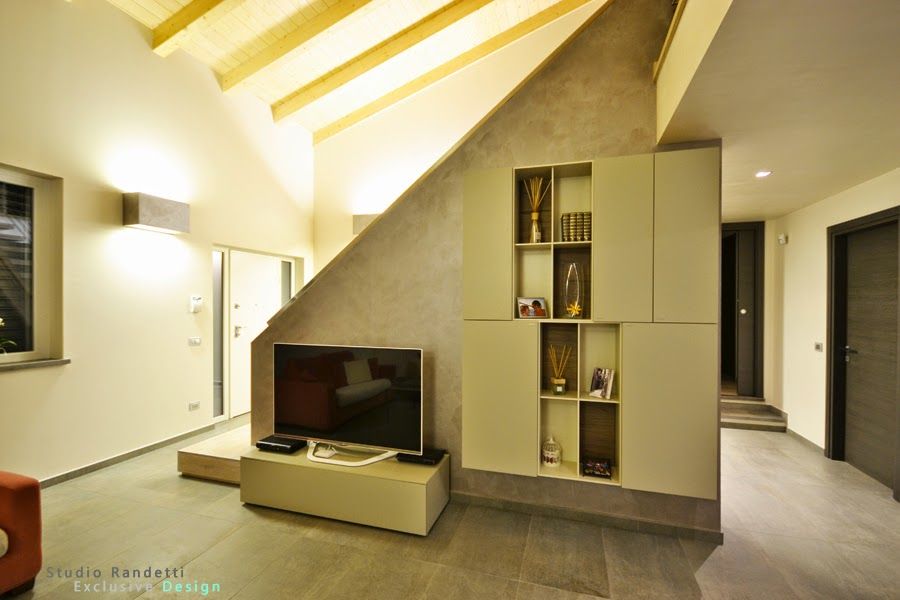 Soggiorno moderno con soffitto inclinato, pareti bianche, mobile TV, scaffalature a muro e corridoio sulla destra.