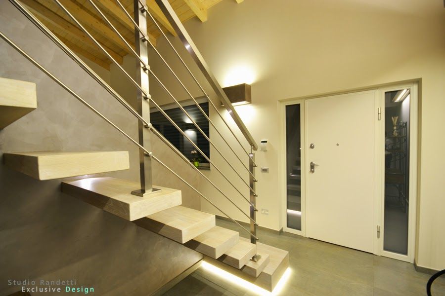Scala interna moderna con ringhiera in metallo accanto a una porta d'ingresso bianca in un corridoio beige.