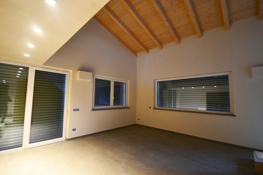 Stanza vuota con soffitto a volta in legno, pareti beige e ampie finestre e porte scorrevoli in vetro.