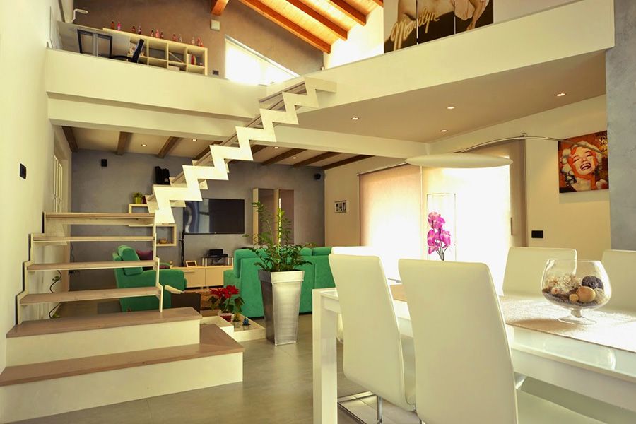 Soggiorno e sala da pranzo moderni a pianta aperta con scala, mobili bianchi, travi in ​​legno e luminosa luce naturale.