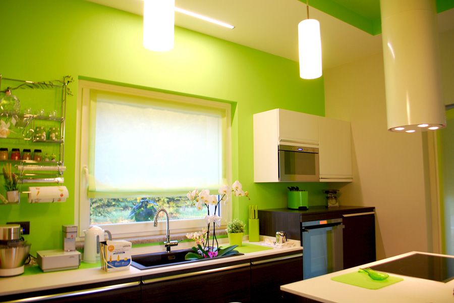Cucina verde lime brillante con lavello sotto la finestra, mobili bianchi e lampade a sospensione.