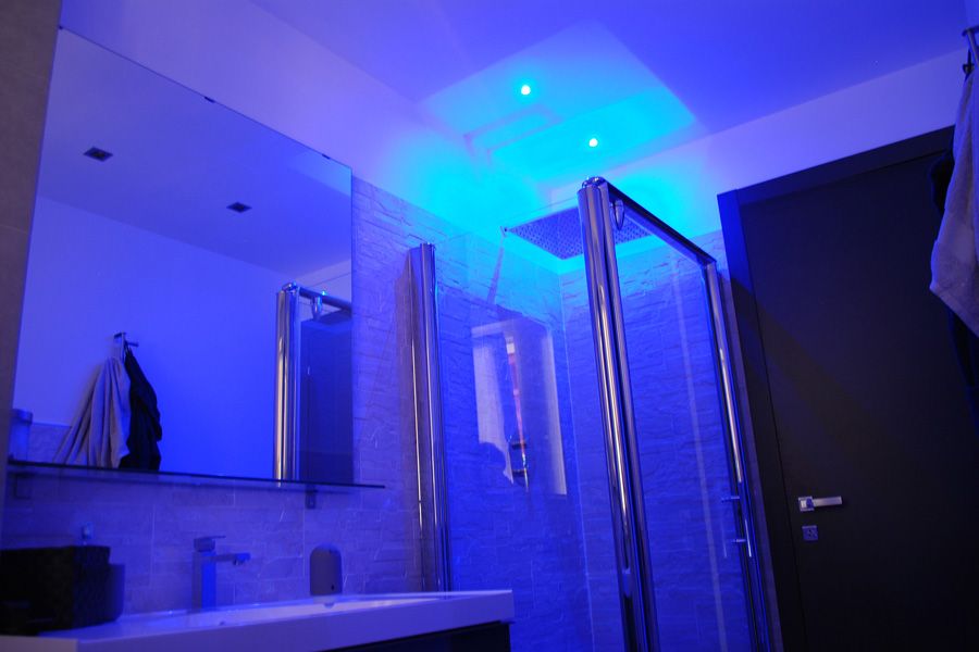 Bagno moderno con luci a LED blu a soffitto, porte doccia in vetro, lavabo, specchio e portasciugamani.
