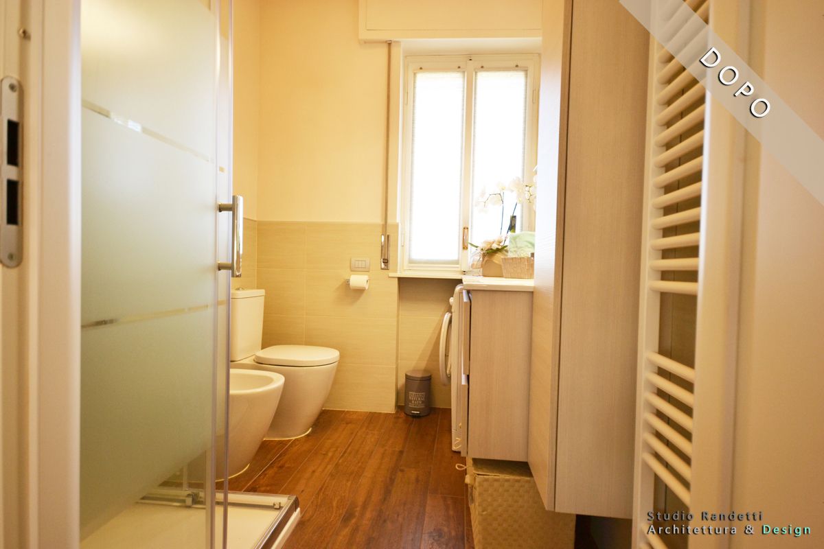 Piccolo bagno beige con WC, lavandino, doccia e finestra sopra un pavimento in legno.