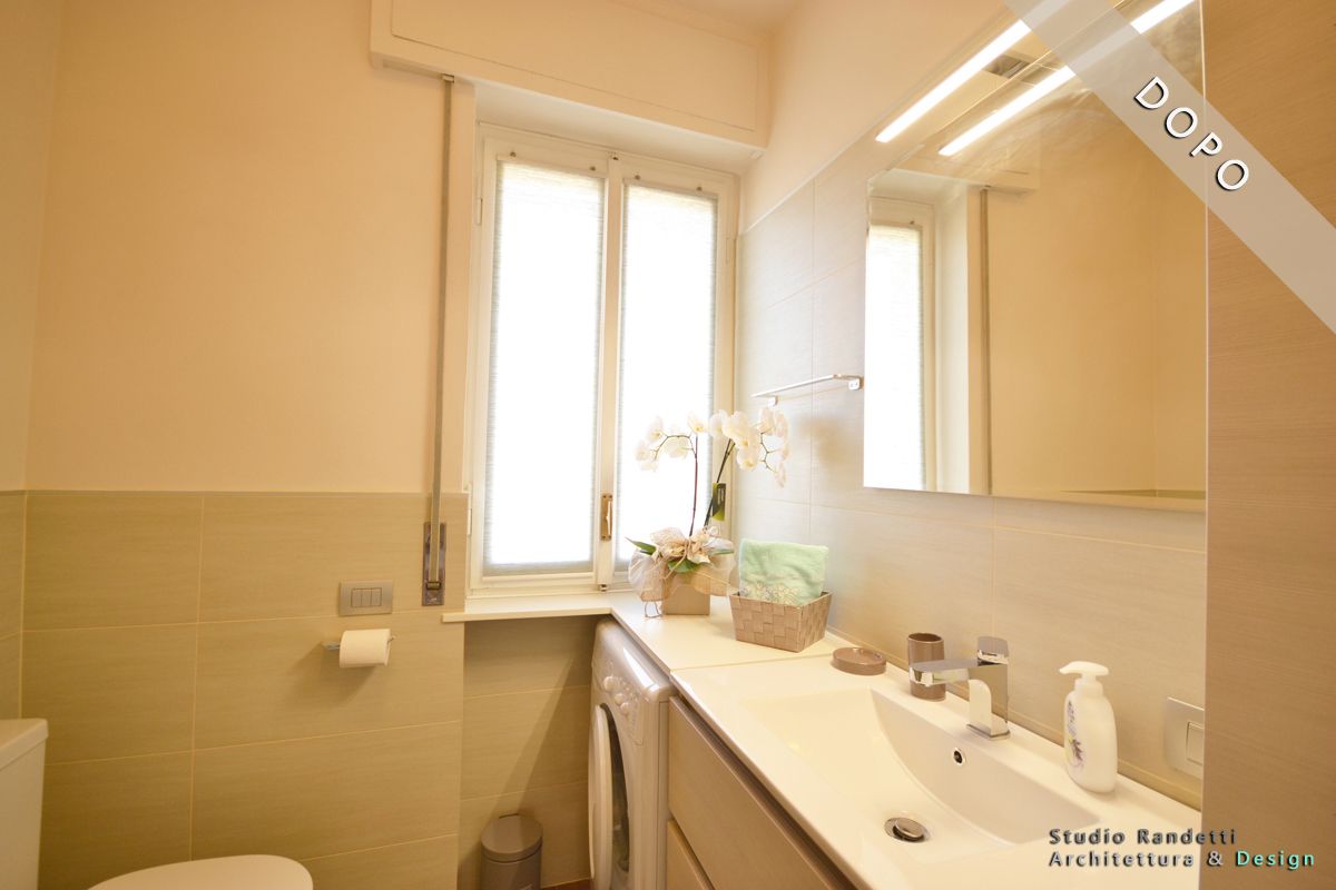 Bagno luminoso con lavabo bianco, specchio, portasciugamani e due finestre alte che diffondono una luce calda.