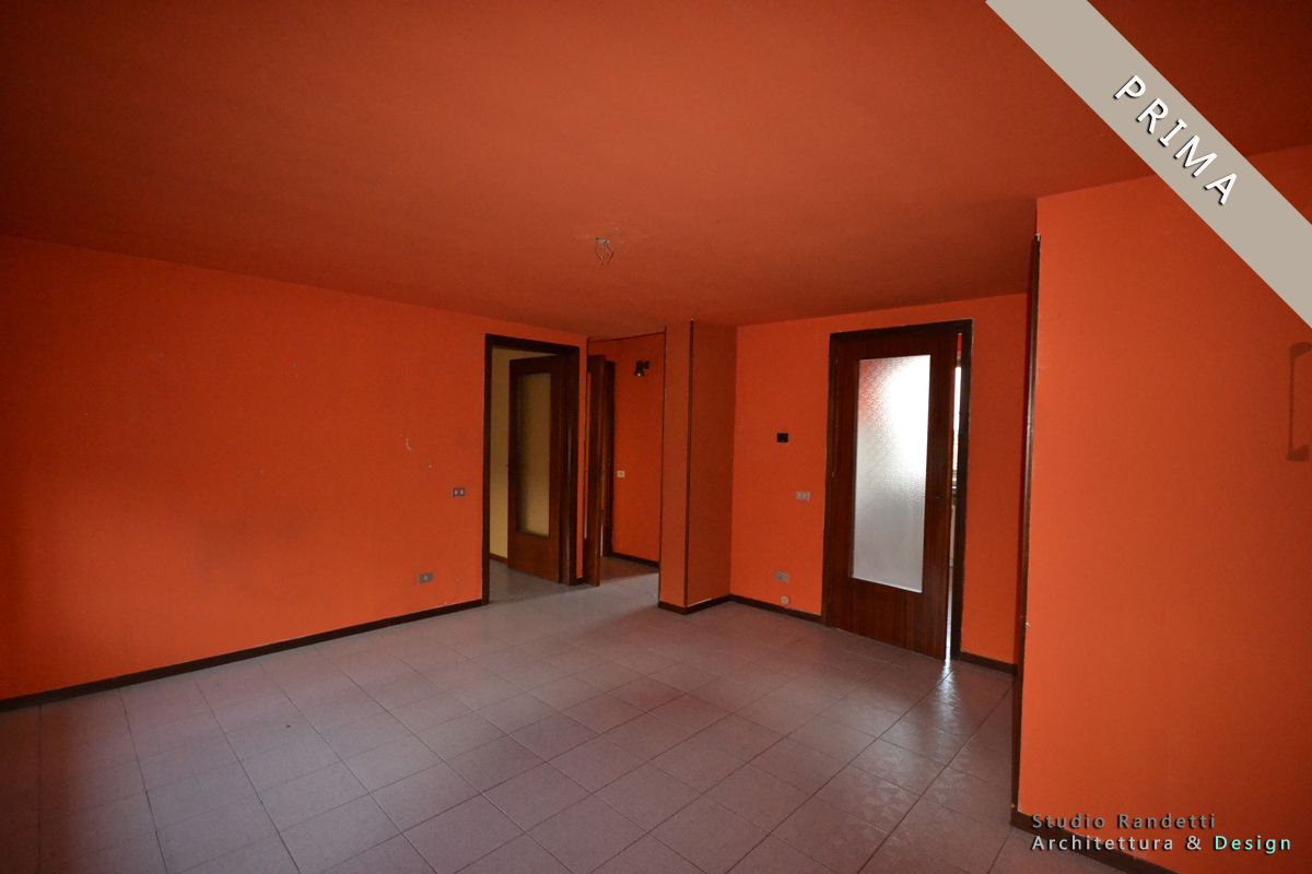 Stanza vuota con pareti arancioni, pavimento in piastrelle grigie e una porta che si apre su un corridoio.