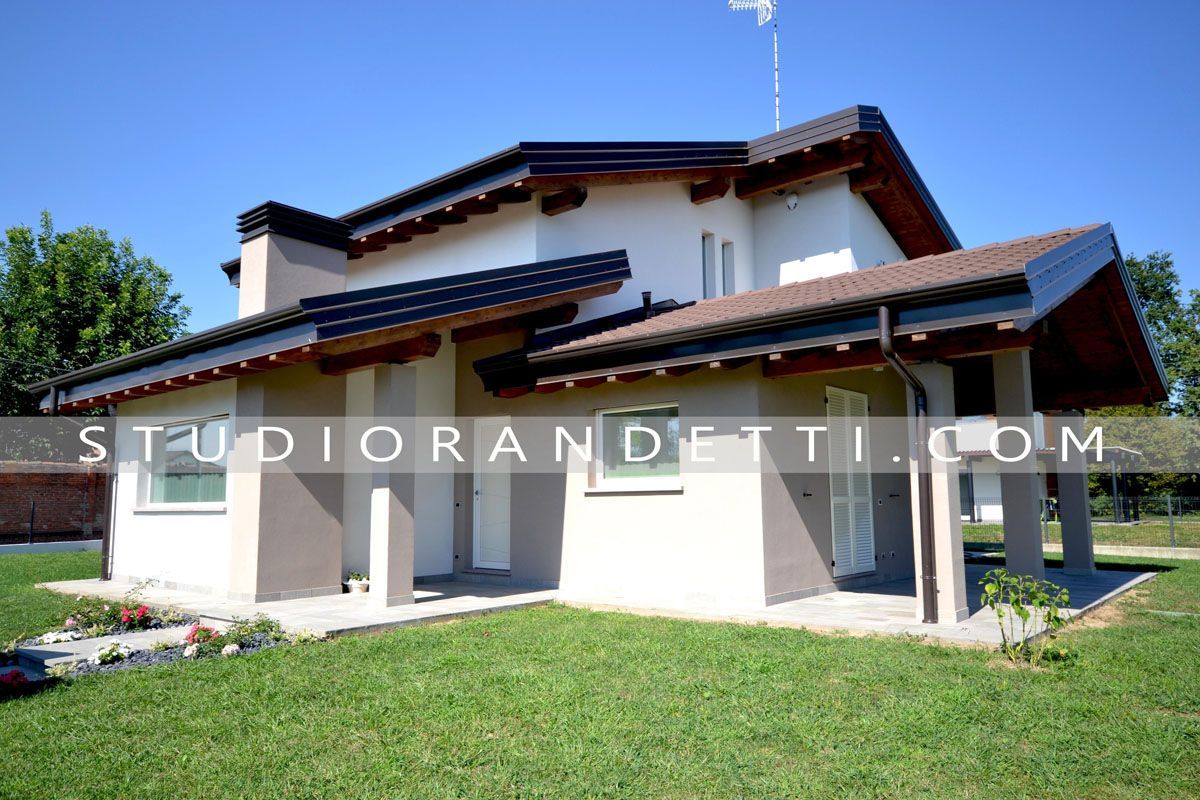 Casa moderna a due piani con pareti bianche, tetto scuro e prato verde sotto un cielo azzurro limpido.