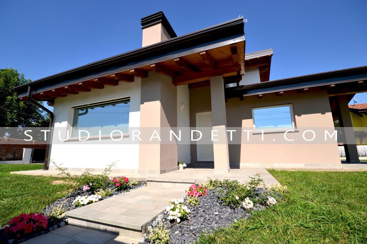 Casa moderna con intonaco beige, ampie finestre e un giardino anteriore curato sotto un cielo azzurro.