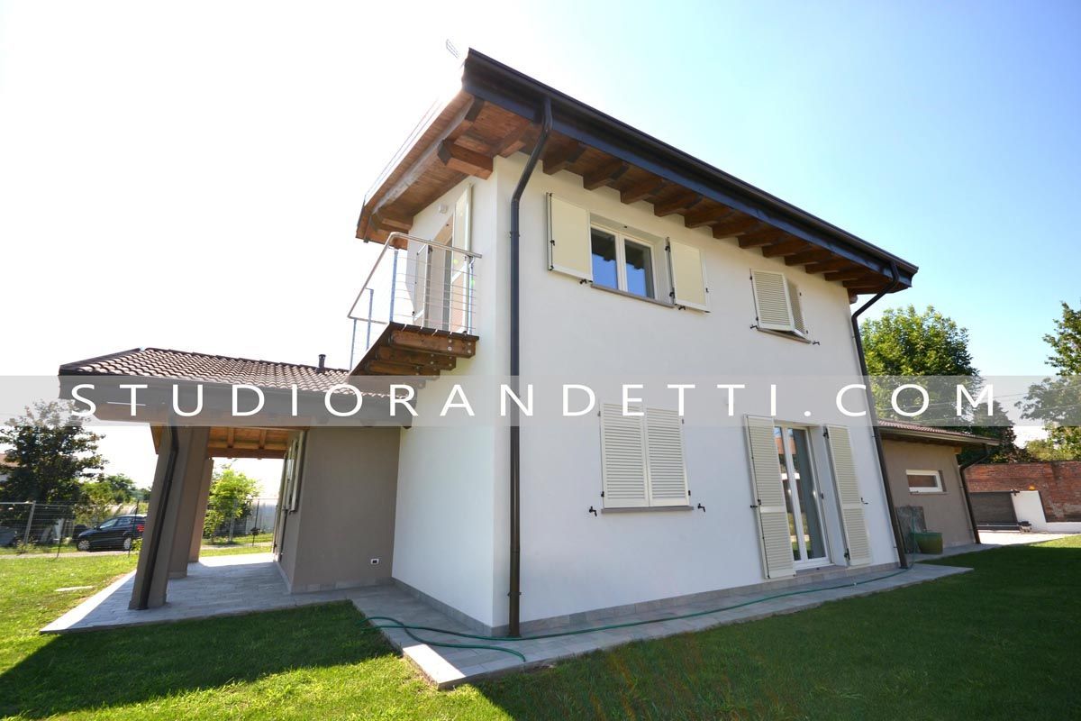 Casa moderna a due piani di colore bianco con dettagli in legno sul tetto e prato in pieno sole