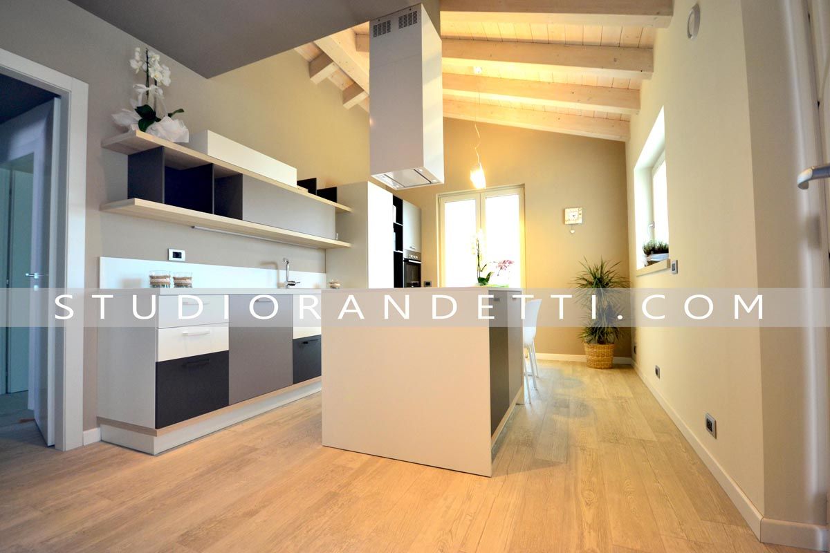 Cucina e soggiorno moderni a pianta aperta con pavimenti in legno chiaro, mobili bianchi e travi a vista sul soffitto.