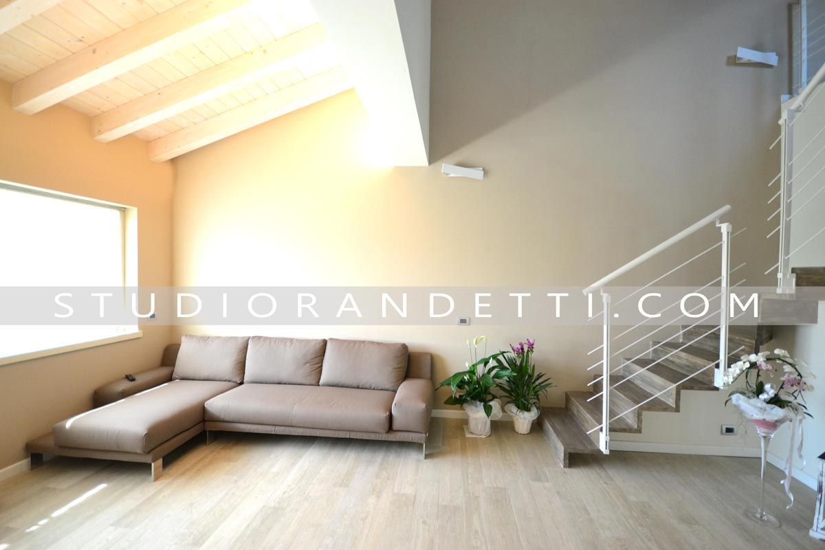 Luminoso soggiorno moderno con divano componibile beige, scala e ampie finestre.
