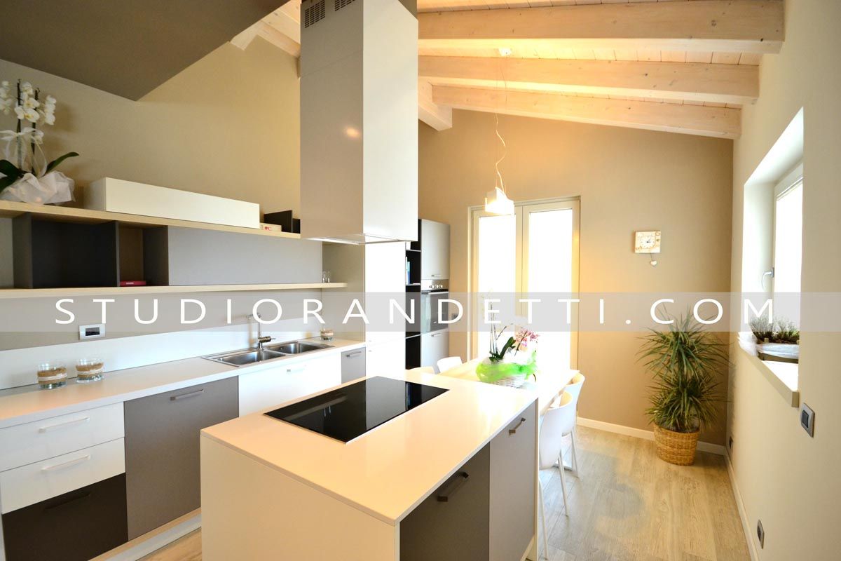 Cucina moderna e luminosa con mobili bianchi, travi in legno, isola centrale e ampie finestre.