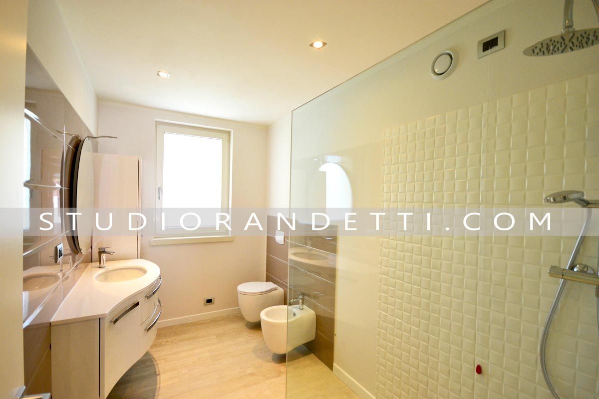 Bagno moderno e luminoso con lavabo, WC, bidet, doccia e pavimento in piastrelle beige.