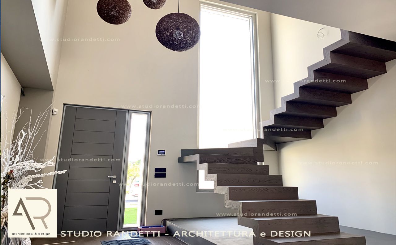 Ingresso moderno con scala scura, porta d'ingresso grigia e ampia finestra con lampade a sospensione.