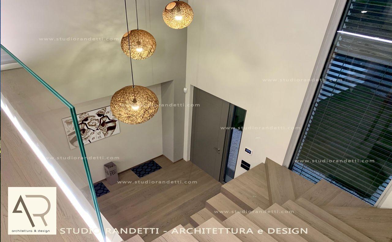 Interno di una scala moderna con ringhiera in vetro, lampade a sospensione e finestre alte.