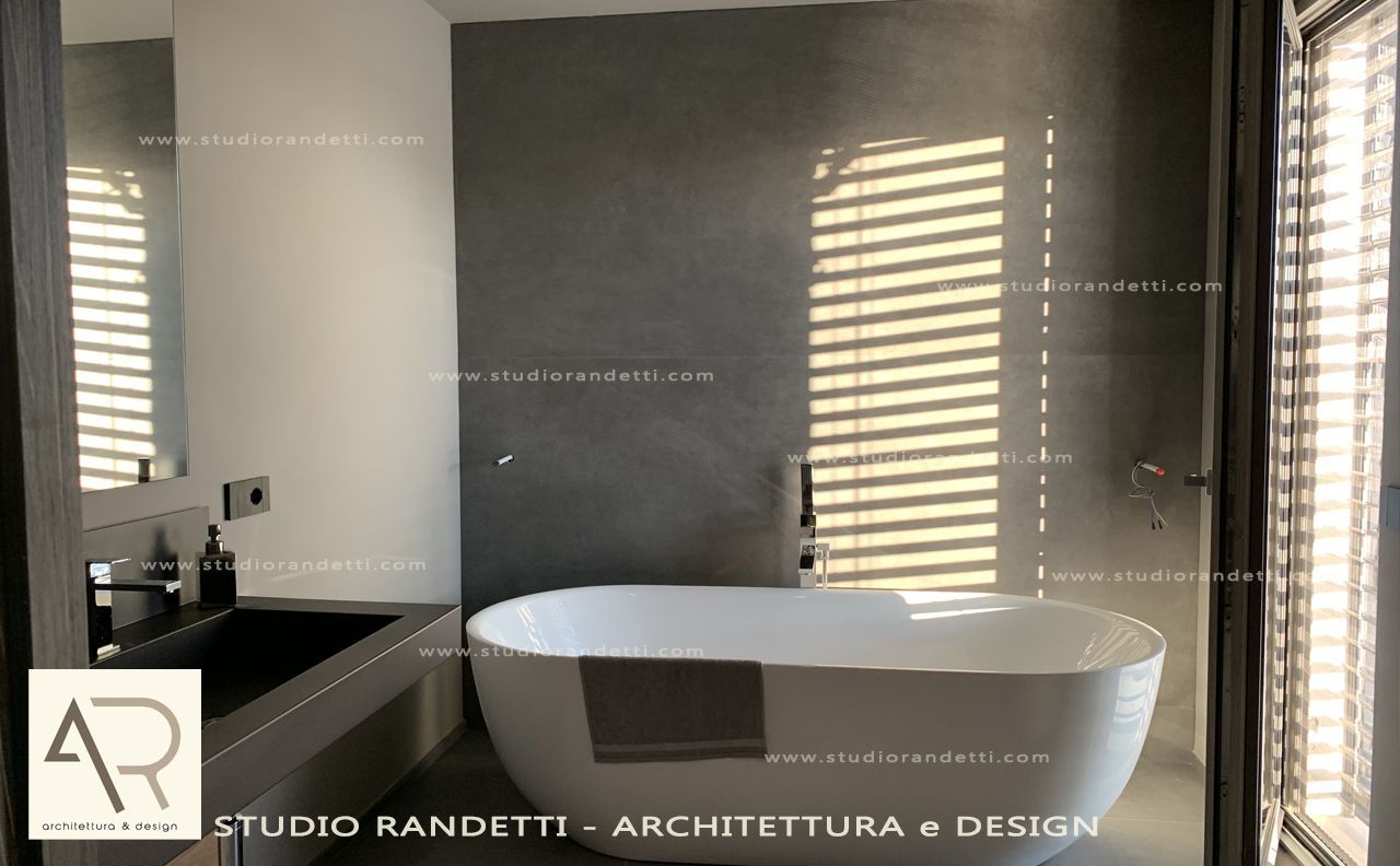 Bagno moderno con vasca ovale freestanding, mobile lavabo scuro, specchio e luce solare filtrata attraverso le tende.
