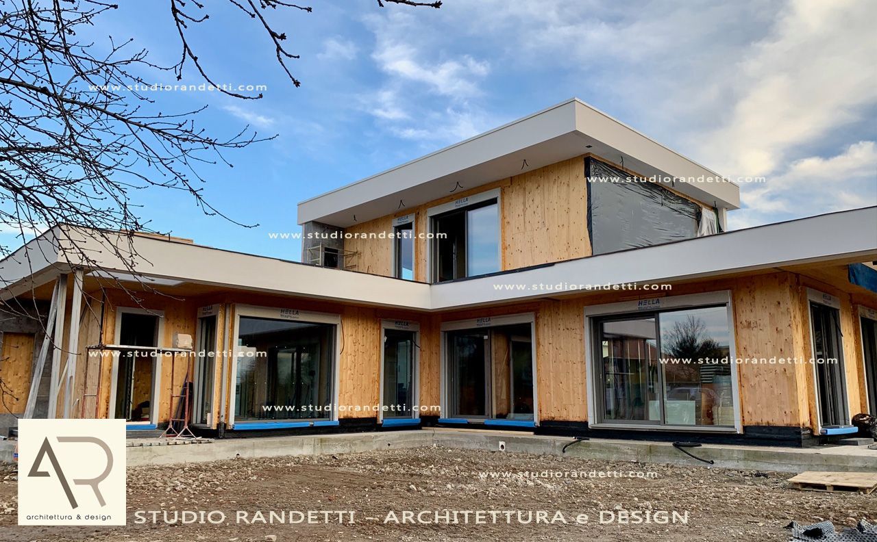 Casa moderna a due piani con rivestimento in legno, ampie finestre e tetto piano sotto un cielo nuvoloso.