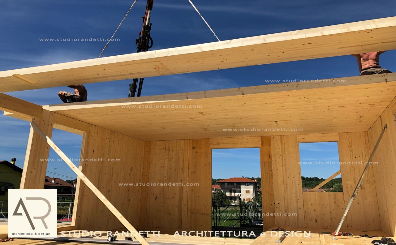 Struttura in legno in costruzione sullo sfondo di un cielo azzurro, con i cavi di una gru che volteggiano sopra.