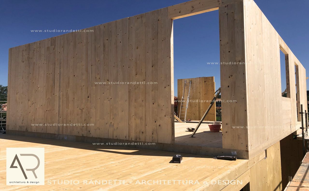 Casa modulare in legno in costruzione su un terreno soleggiato, con ingresso aperto e pareti non rifinite.